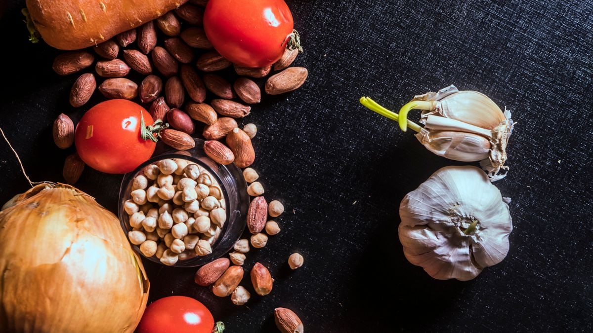 Top view of fresh vegetables and nuts arranged on a dark surface, showcasing raw ingredients.